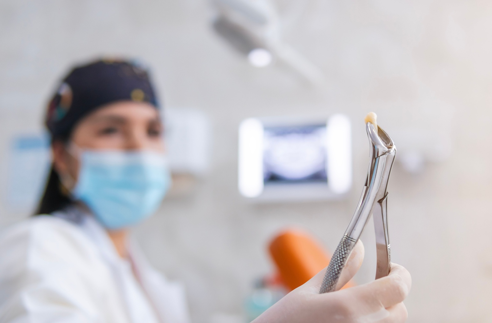  A dentist in the background holds an extracted tooth with gripping forceps.